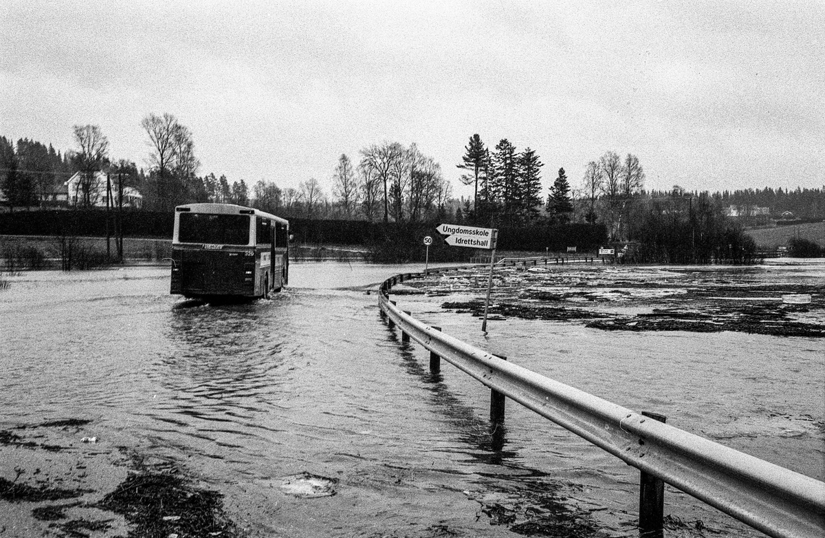 Flomskader på veiene, Riksvei 120, Ytre Enebakk. Vannet flommer over veier og jorder, biler kjører så vannspruten står.