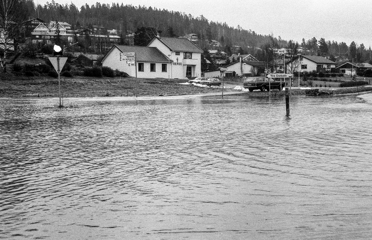 Flomskader på veiene, Riksvei 120, Ytre Enebakk. Vannet flommer over veier og jorder, biler kjører så vannspruten står.