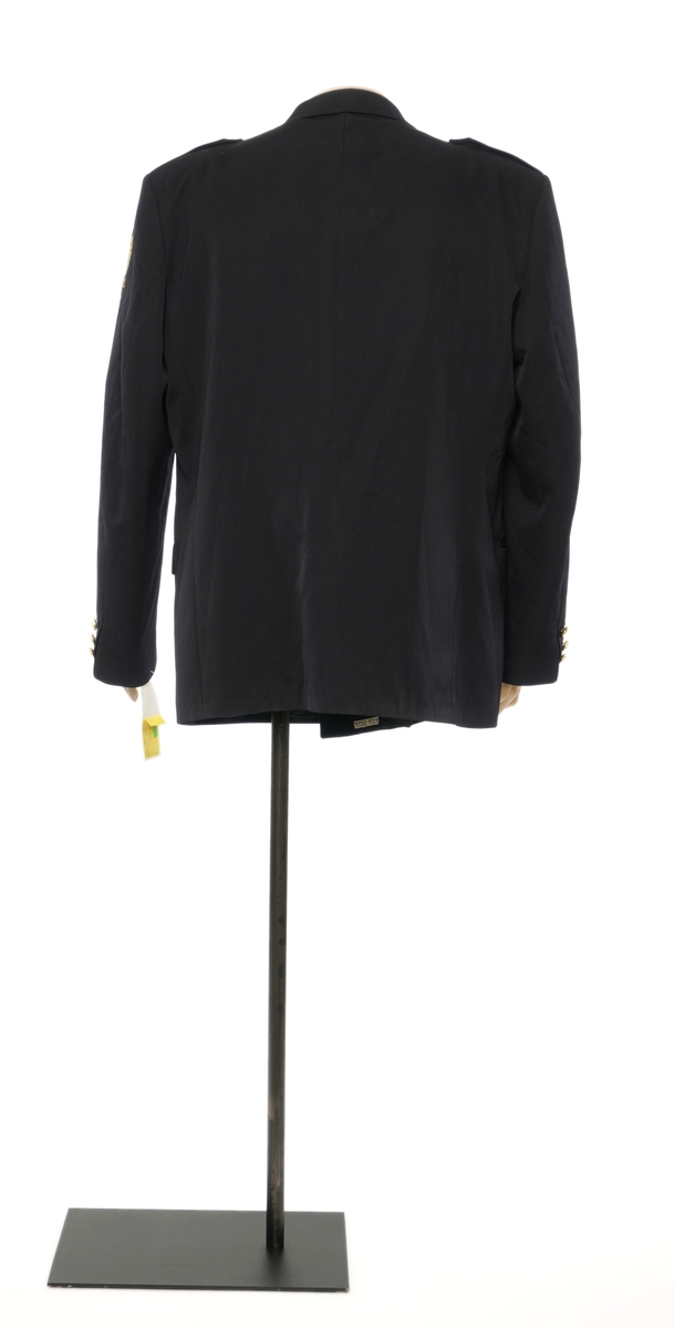 Mørkblå jakke enkelspent med tre riksløveknapper. Epauletter uten distinktsjoner. Tekstil marke på venstre arm, riksløve med hvit øks omgitt av eikeblader over TOLL. Hempe i nakke. Kypert stoff, blanding av polyester og ull. Jakke er foda med antatt syntetisk stoff, mørkblå.
Bukser av samme stoff.