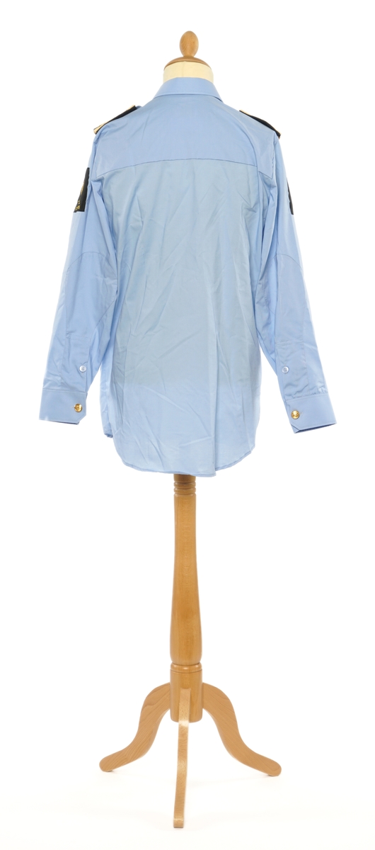 Lys blå langermet skjorte av et fintvevd stoff. Epauletter med tilsatt distinktsjon: krone over merkurstav over en kvist eikeblader (fire blader totalt), med gull bånd på begge sider. Tekstil merke på begge armer: krone over riksløve med hvit øks i rødt skjold omgitt av eikeblader over TOLL/CUSTOMS.