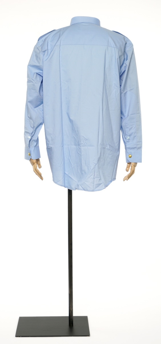 Lys blå  langermet skjorte av et fintvevd stoff. Epauletter uten tilsatt distinktsjon. Tekstil merke på venstre armen: riksløve med hvit øks omgitt av eikeblader over TOLL.