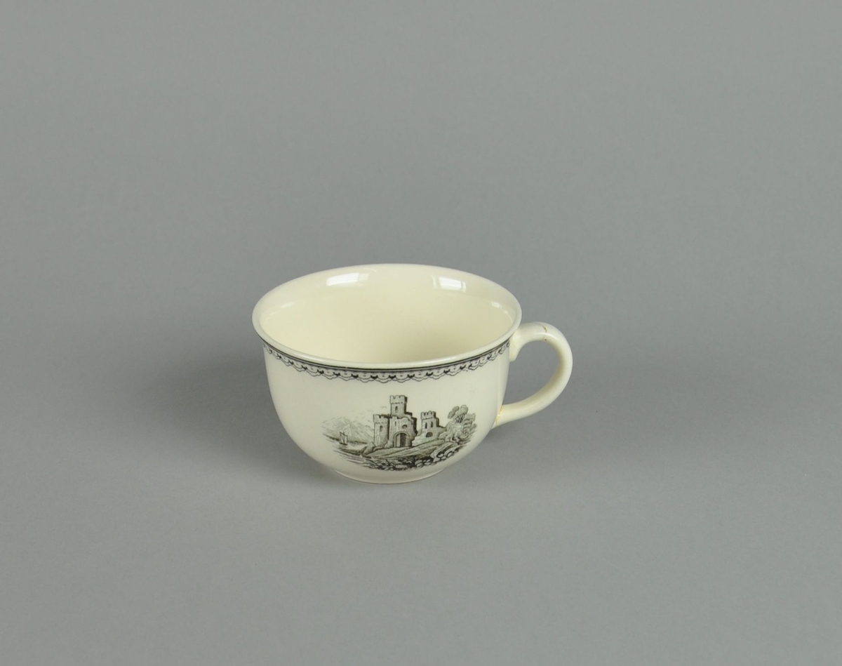 Kopp av glassert keramikk, med hank. Svart dekortrykk av klosterruiner og gård, samt en borde langs randen. Hanken har vært knekt av og limt på igjen.