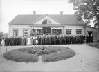 Stort middagssällskap framför prästgården i Norra Vi. Skälet är installationen av Reinhold Wester som ny kyrkoherde i socknen. Wester ses stående längst fram i ledet. Den andre mannen till vänster om Wester är den skäggprydde biskopen Johan Personne. Året är 1923.