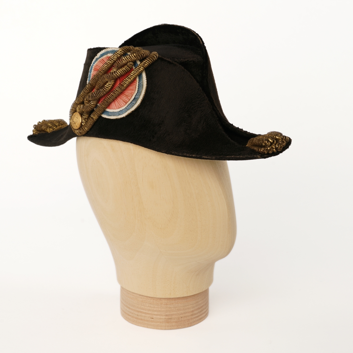 Snutehatt av sort, velurlignende stoff. Rød-hvit-blå kokarde, gulltresse med riksløveknapp. Gullpynt i hver snute. Brunn skinn til svetterem, lys lilla silkefôr. 
Metall hatteske til snutehatt.