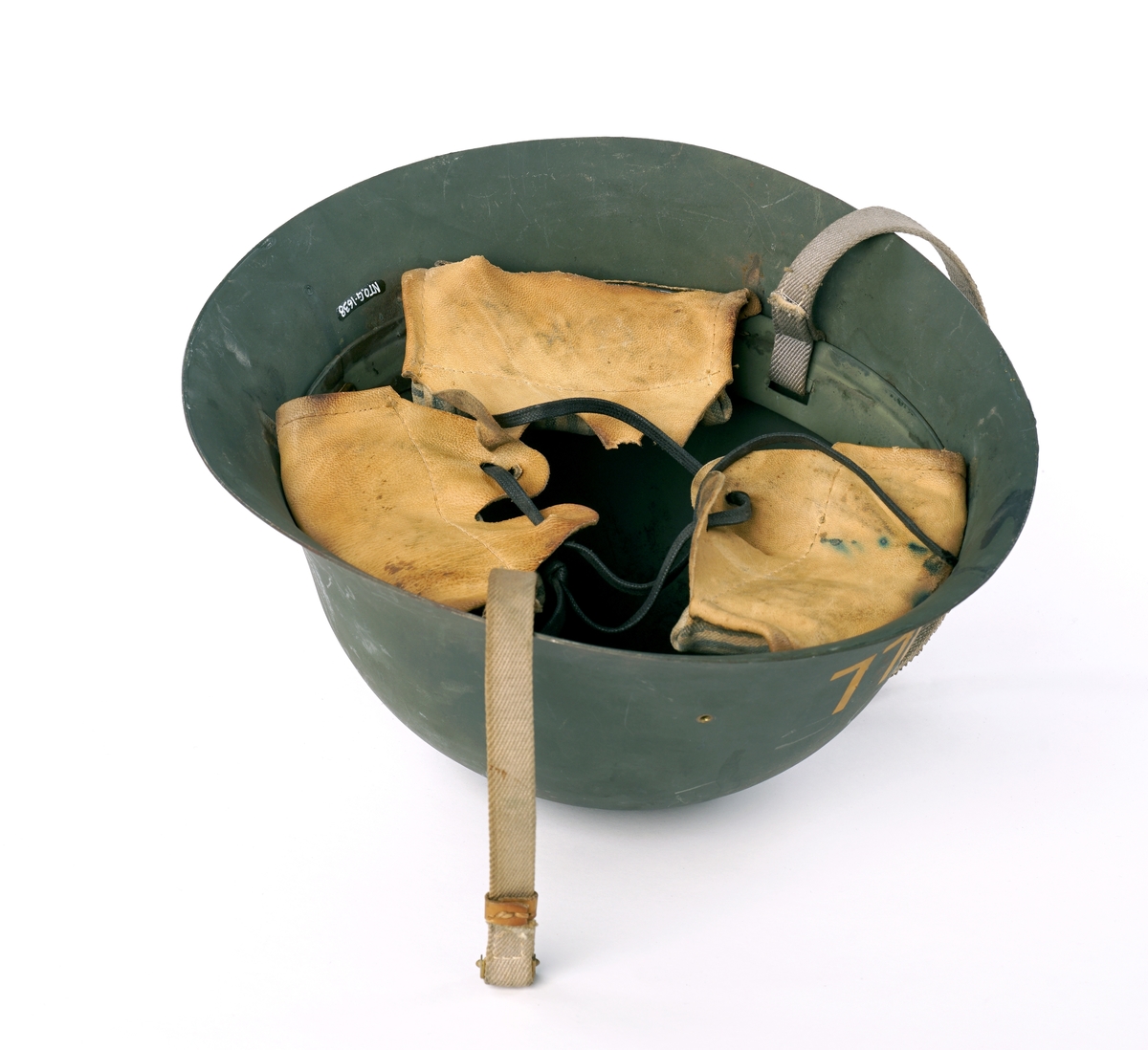 Metall hjelm (magnetisk), grønnmalt med 'TOLL'  stensilerte i gul maling. På innsiden, tre lær klaffer med puter på innsiden, forbundet med en sirkel av snor å justere for hodestørrelse. Tekstilbånd på hver side, en med metalllås for lukking under haken.