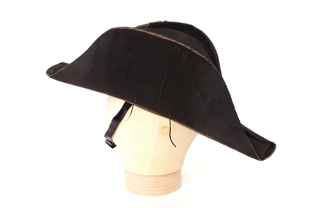 Snutehatt av sort, velurlignende stoff. Rød-hvit-blå kokarde, krysset med sortbånd festet med riksløveknapp. Fire tynne sorte snorer på hver side. Rødt skinn til svetterem, hvit silkefôr. Hvit knapp i toppen av innsiden pull. Sort lær hakerem.
Metall hatteske til snutehatt.