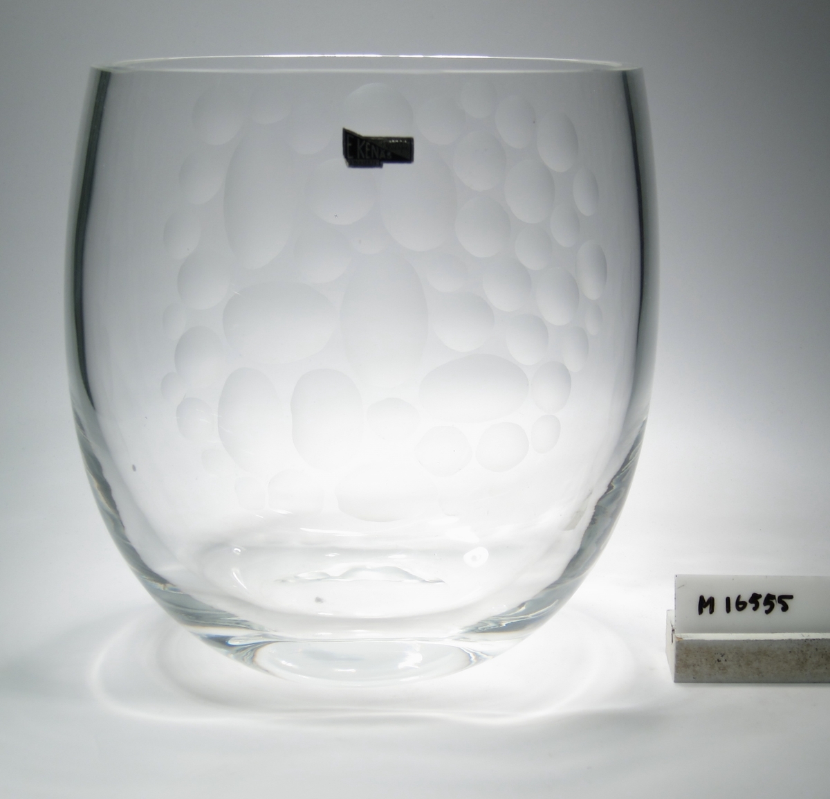 Vas.
Formgiven av Johan-Orwar Lake.
Beskrivning: Dekor i form av inslipade, matta ovaler.
Färg: Ofärgat klarglas.
Mått: Ovan anges höjd, övre diameter samt djup. Diameter botten: 80 mm.
Märkning: Etikett med text. Se "Signering, märkning" ovan.
Inskrivet i huvudkatalogen 1958.

Se även M 16556.
Funktion: Vas