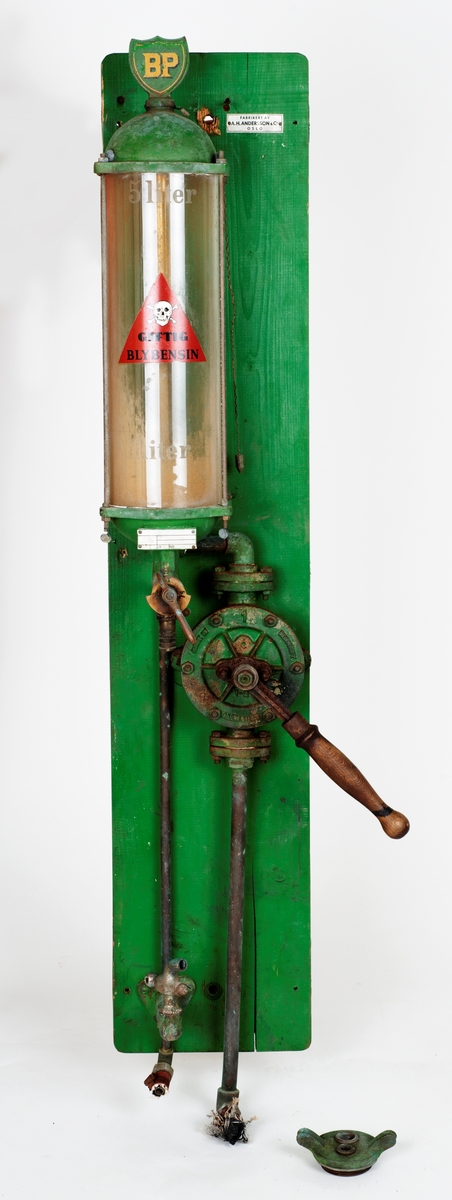 Oljepumpe med ventil montert på blå treplate. Tanken tar 5 liter. Feste for å sette en kanne e.l. under tanken. 

Ventil er produsert i UK, merke Runwell No 0
Oljepumpe fra Norsk Brendselsolje. Dette ble senere Noroil og deretter Statoil. Se: https://no.wikipedia.org/wiki/Norol