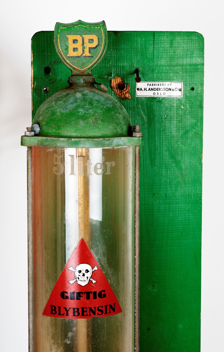 Oljepumpe med ventil montert på blå treplate. Tanken tar 5 liter. Feste for å sette en kanne e.l. under tanken. 

Ventil er produsert i UK, merke Runwell No 0
Oljepumpe fra Norsk Brendselsolje. Dette ble senere Noroil og deretter Statoil. Se: https://no.wikipedia.org/wiki/Norol