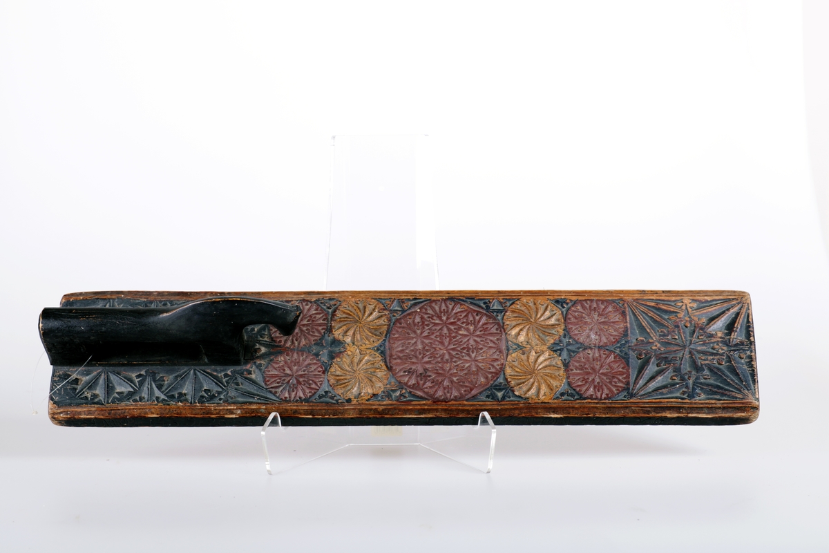 Mangletreet er malt sort, rødt og gull. Karveskur, med store og små seksbladsroser og buestjerner. Inskripsjon: anno 1743, dato 26 februar. Nils Øistensøn Marsta. Hestehåndtak.