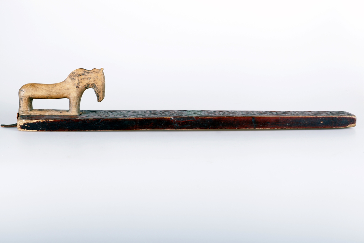 Mangletreet er malt rødt med to gule rosetter. Dekortert med store og små rosetter med seksbladsroser, og sikksakkbord ved håndtaket. Hestehåndtak. Datert 1804. Håndtaket er nyere og trefarget. Lærhempe i enden.