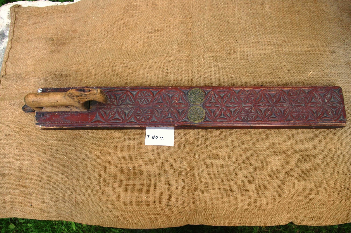 Mangletreet er malt rødt med to gule rosetter. Dekortert med store og små rosetter med seksbladsroser, og sikksakkbord ved håndtaket. Hestehåndtak. Datert 1804. Håndtaket er nyere og trefarget. Lærhempe i enden.