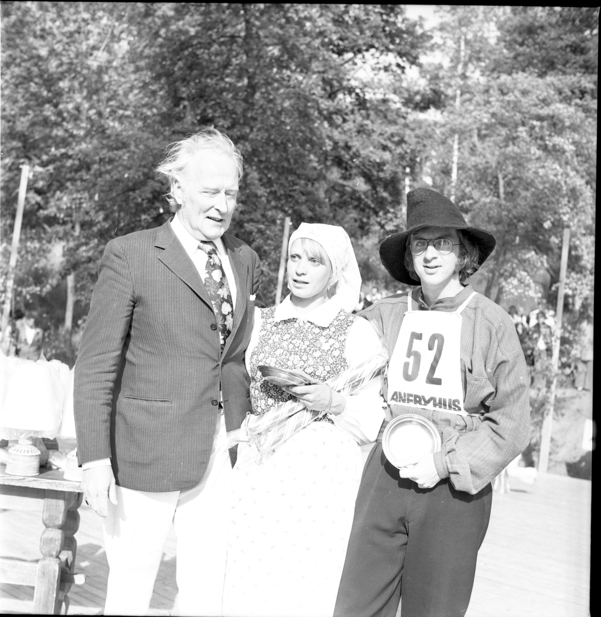 Grännapolkan på Grännaberget, 1975. Danspar nr 52, troligen segrarna Gunnel Johansson och Ola Holmberg från Uppsala intill man som troligen är prisutdelare. Dansparet har tennfat och stor polkagris i famnen.