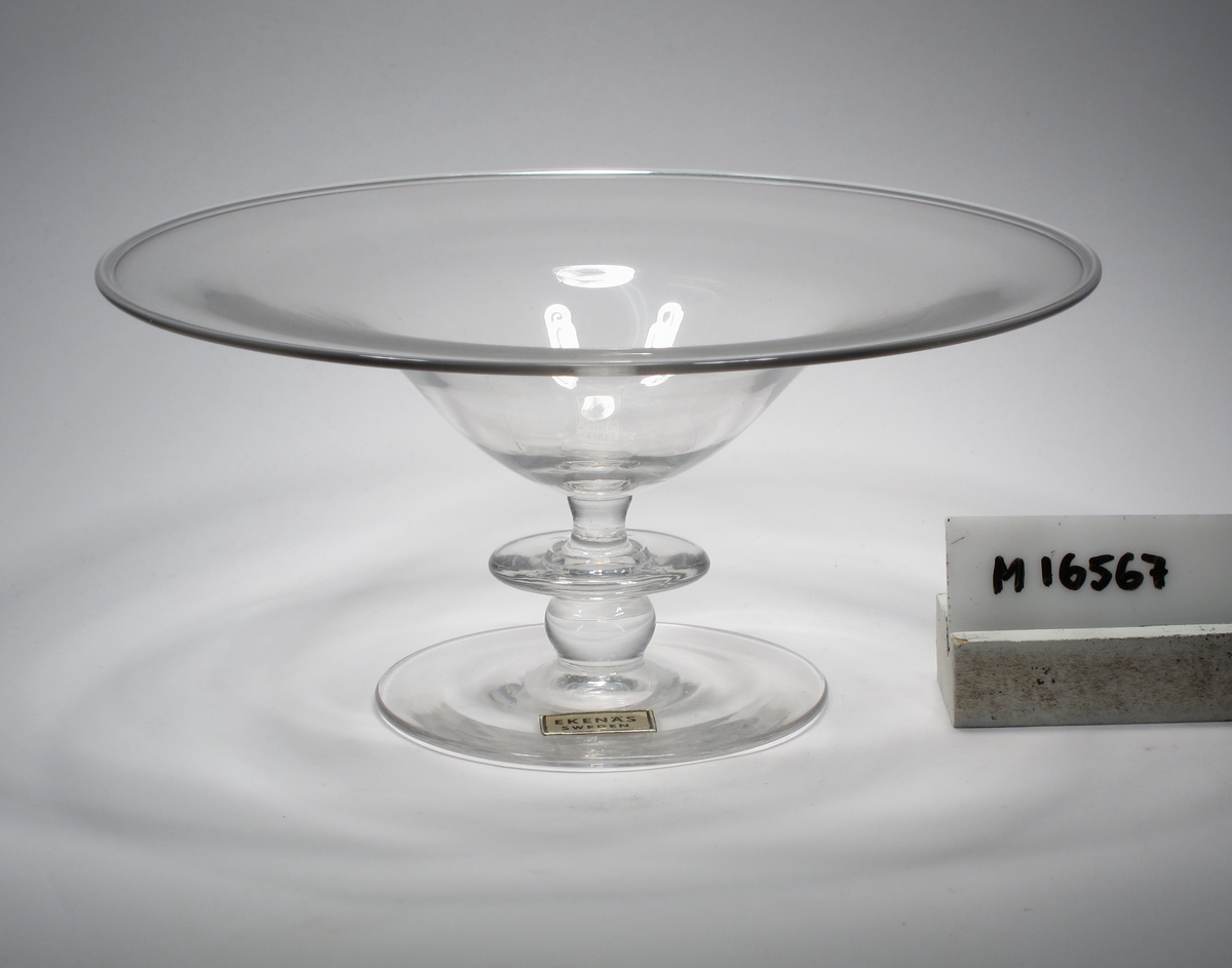 Skål.
Beskrivning: Flat skål på fot.
Färg: Ofärgat, klarglas.
Mått: Ovan anges höjd samt största diameter. Diameter fot: 81 mm.
Märkning: Etikett, rektangulär och guld-svart. Se "Signering, märkning" 1 ovan.
Lapp under foten. Se "Signering, märkning" 2 ovan.
Inskrivet i huvudkatalogen 1958.
Funktion: Skål