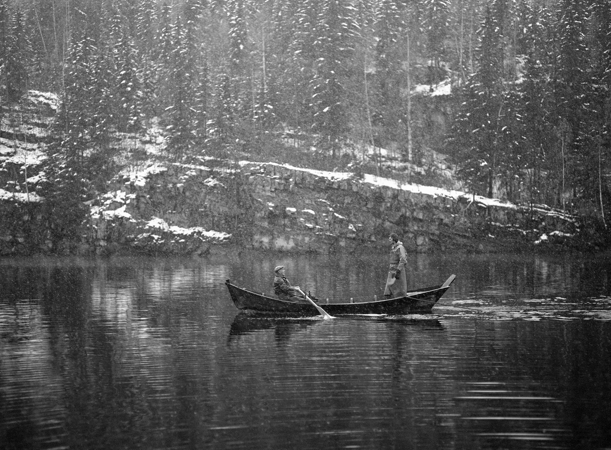 To fiskere i en robåt, ei åfløy, ved Lortvarpet i Fåberg, altså i Gudbrandsdalslågens nedre del.  Fotografiet er tatt en grå oktoberdag i 1976, med sludd i lufta.  Karene var i ferd med å innlede et notkast etter lågåsild (Coregonus albula).  Åfløya var en lokal båttype, som flatbotnet, bred og kraftig kuvet i lengderetningen og et sterkt utfallende akterparti («plitten»). Nota var et bundet, finmasket innstengingsredskap.  Den hadde kraftig tauverk øverst og nederst, henholdsvis «flætennol» og «søkketennol», som var utstyrt med henholdsvis flyteelementer og søkker.  Dermed ble det finmaskete garnet – «bundingen» – stående som en vegg i vannmassene.  I begge endene av bundingen var det tau, som ble brukt når nota skulle dras mot land.  Her var brødrene Martin og Sæming Søreng klare til å foreta et notkast.  Martin var «sættar».  Han satt ved årene og skulle ro båten i ei bue ut i elveløpet og deretter inn mot land igjen.  Broren Sæming var «bøler» og skulle kaste fangstredskapen i vatnet.  Da bildet ble tatt hadde karene i båten overlatt enden av «stillpinntauet» til en eller flere karer på land, og bøleren sto oppreist i båten, klar til å begynne å kaste sjølve notveven i vatnet.  Lengre nede ved elvebredden sto en eller flere karer klare til å ta imot «åfløytauget» eller «innreiingstauget».  Ved Lortvarpet skal begge tauene ha vært om lag 150 meter lange.