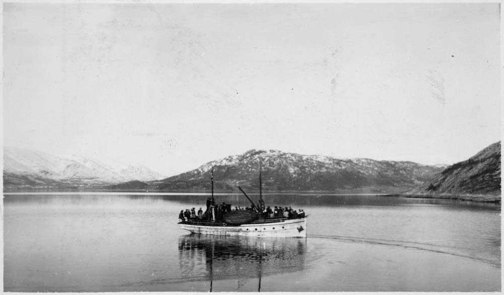 Masse folk ombord i en fiskebåt i Vefsna, på tur til skitur. Man kan se Holandsvika til venstre, Rynes til høyre.