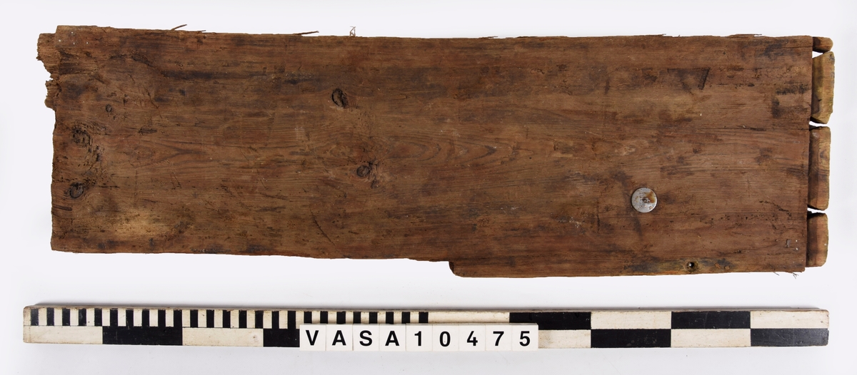 Fragment till en rektangulär bräda med väl bevarade laxstjärt stycken på ena ände. En avbruten sink på den andra ände. 2 spikhål med huvudspår längs en långkant.
det Original föremålet var dubbelt längd - avbruten längs sinket. Avbrytningar och kraftig vittring på långkanter.