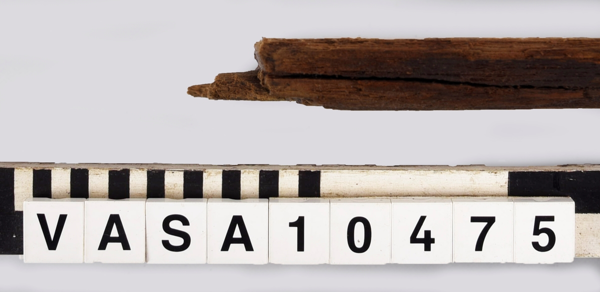 Fragment till en rektangulär bräda med väl bevarade laxstjärt stycken på ena ände. En avbruten sink på den andra ände. 2 spikhål med huvudspår längs en långkant.
det Original föremålet var dubbelt längd - avbruten längs sinket. Avbrytningar och kraftig vittring på långkanter.