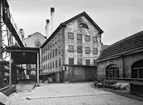 Miljön vid Malcolms ångkraftcentral i Norrköpings industrilandskap. Odaterad bild som bär 1950-talets prägel. I bakgrunden skymtar den så kallade Värmekyrkan som bevarats in i vår tid i ny funktion som konsertlokal. Ursprungliga försåg byggnadens koleldade ångpannor industrierna i området med värme och ånga. Den äldsta delen uppfördes i två etapper 1927 och 1930 efter ritningar av arkitekt Ivar Tengbom. Vy mot sydost.