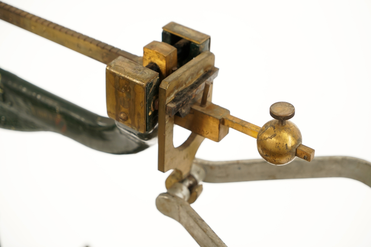 Balansevekt av metall bestående av fot,ben,vektarm og vektskål.