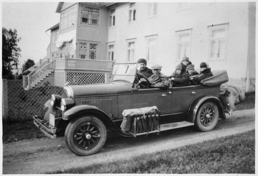 Flere personer i en Chrysler Roadster (1928 modell?) med stort hus i bakgrunnen. W-27 registrert på Gunnar Wikborg Vik som også er sjåføren på bildet.