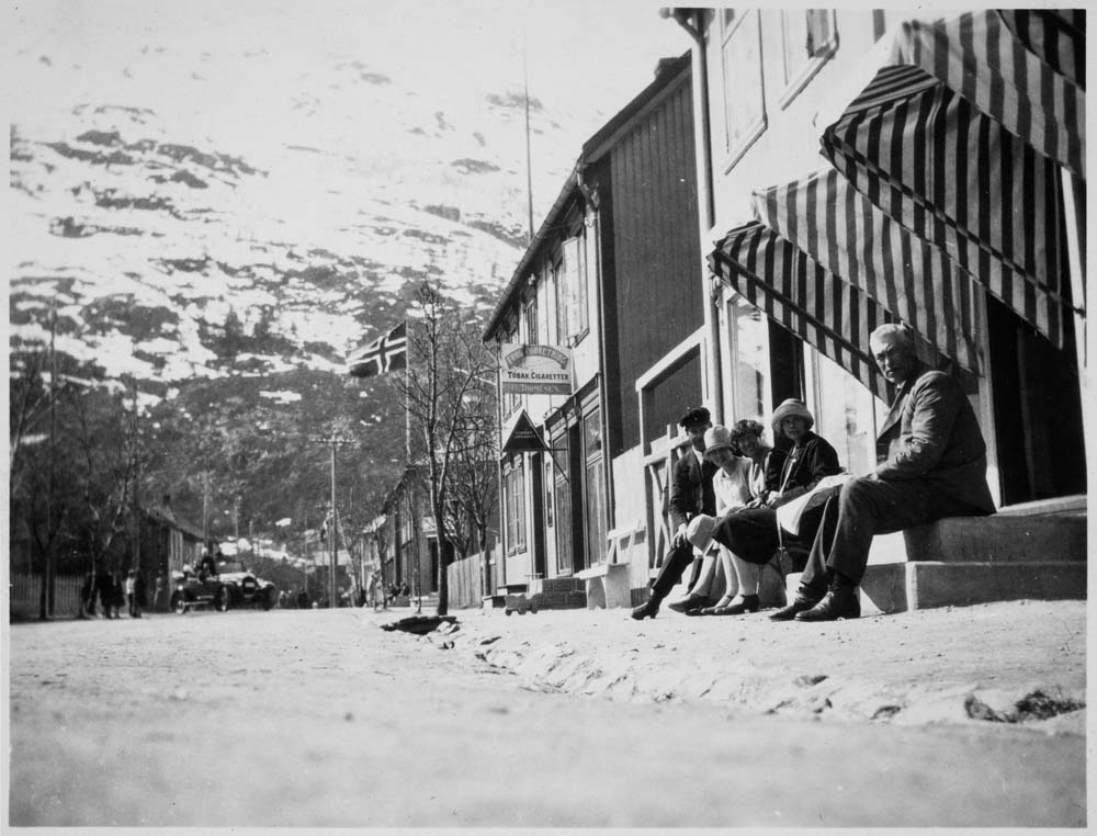 Flere personer sitter på en trapp i Mosjøen. Flagg og Øyfjellet i bakgrunnen.