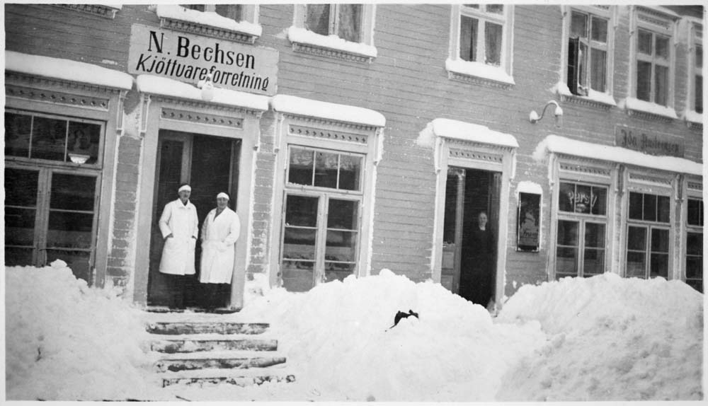 Vinterbilde. N. Bechsens kjøttvareforretning i Sjøgata. To personer i hvite frakker i døra.
