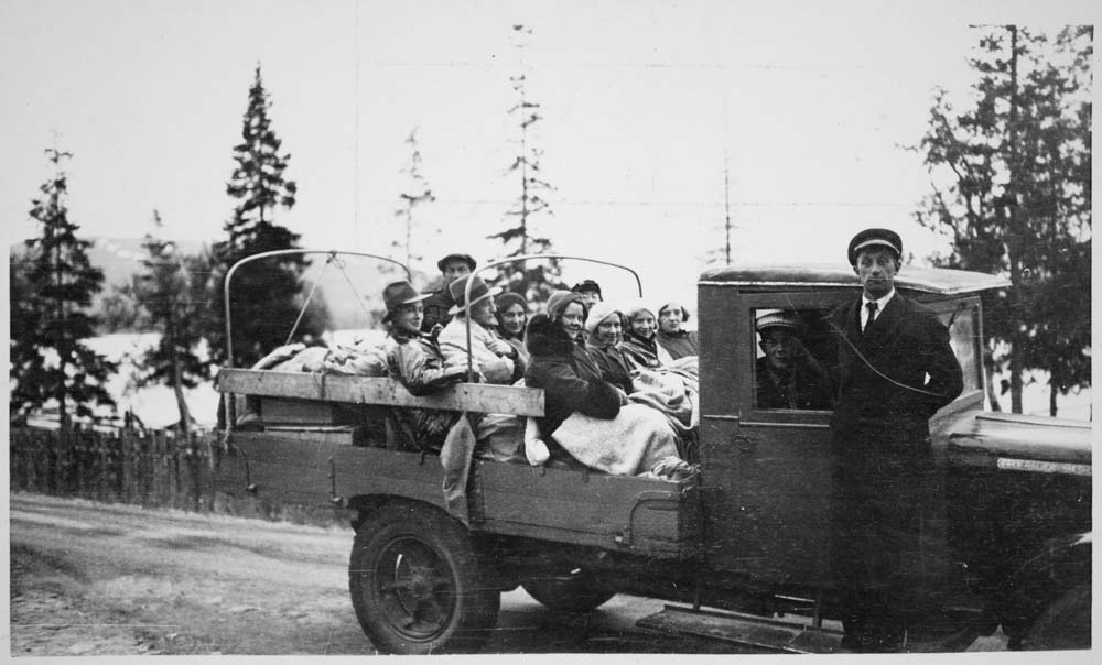 Lastebiltur. Ni personer på lasteplanet. Sjåfør står oppstilt ved lastebilen og en person sitter inni.