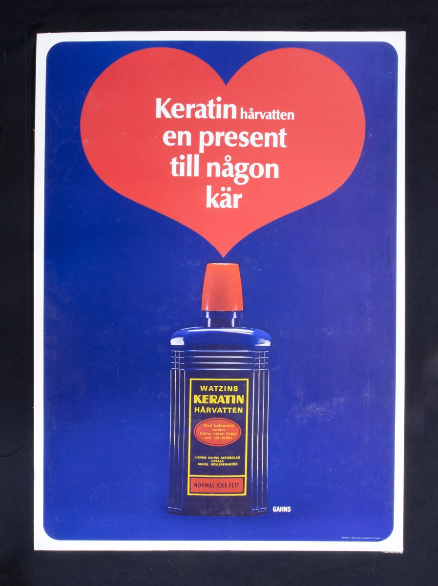 Reklamskylt i papp för hårvatten. På bilden finns en flaska hårvatten med ett hjärta ovanför den.
Text: Keratin hårvatten en present till någon kär.