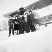 Gruppfotografi av flygare från F 19 samt två kvinnor framför flygplan Gloster Gladiator på ett flygfält på Kyrksjöns is i Ljusdal den 3 januari 1940. Från vänster Martin Wennerström, okänd kvinna, Hans Olof Palme, Einar Tehler, Åke 