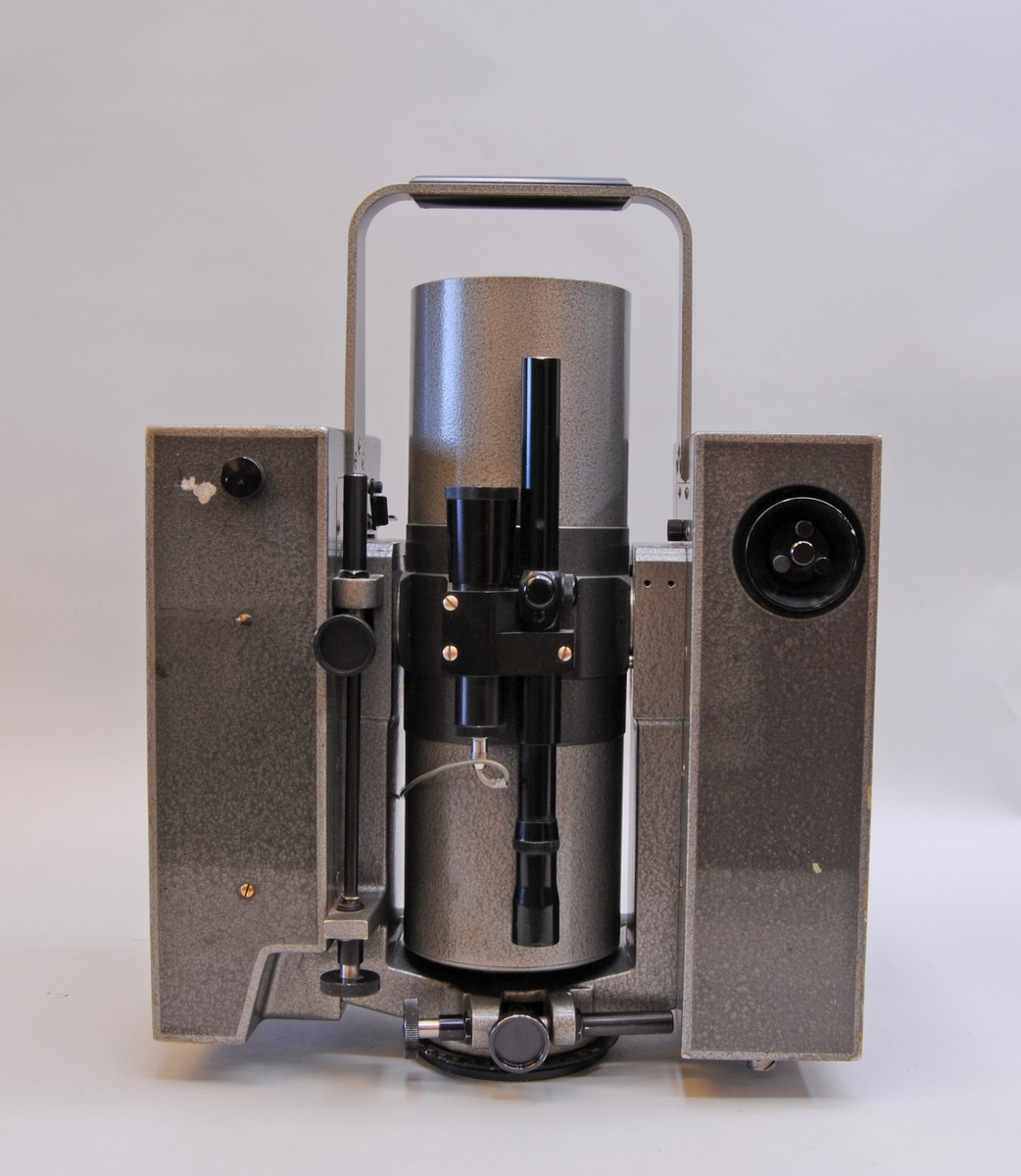 AGA Geodimeter modell 6. Mätinstrumentet har ett grått plåthölje. I mitten av instrumentet finns en cylinderformad tub som går att vinkla till horisontellt läge och skruvas åt för att fastsättas. På sidorna om tuben är två rektangulärt stående partier med olika reglage på den sidan som instrumentet manövreras från. Instrumentet står på en rund vridbar platta som är avsedd att fästas i ett stativ. Se även fodral Jvm23132:2-3 samt tillbehör Jvm23132:4-9.