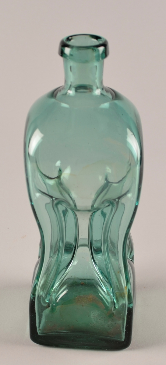 Flaske i lys grønt glas. Fire sider, der det er "knipe" inn midt på sida i kvart hjørne, slik at det vert fire smale røyr i kvart hjørne og i mdoten av flaska som væska i flaska renn gjennom ved skjenking. Likesida.