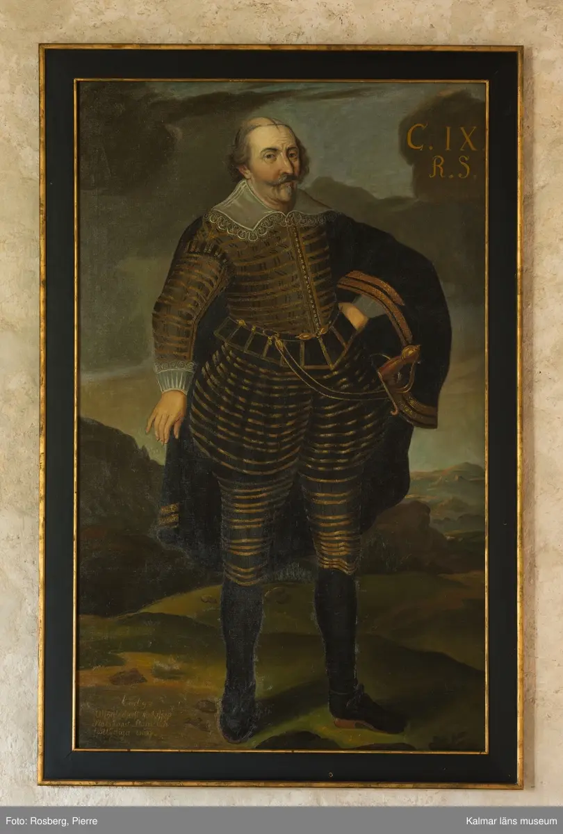 Karl IX i helfigur, stående, i mörk dräkt med guldstickningar, mantel med guldbroderier, spetskrage samt spetsar vid handlederna. Värja, svarta strumpor och skor med spännen.