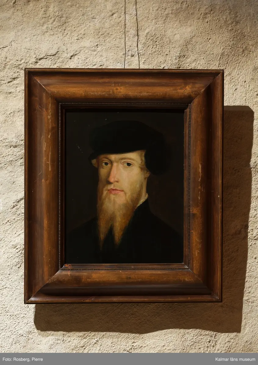 Erik XIV avbildad i bröstbild, face vänster, med svart rock med liten vit spetskrage som precis skymtar och svart barett. Tudelat skägg. Umbrafärgad bakgrund.