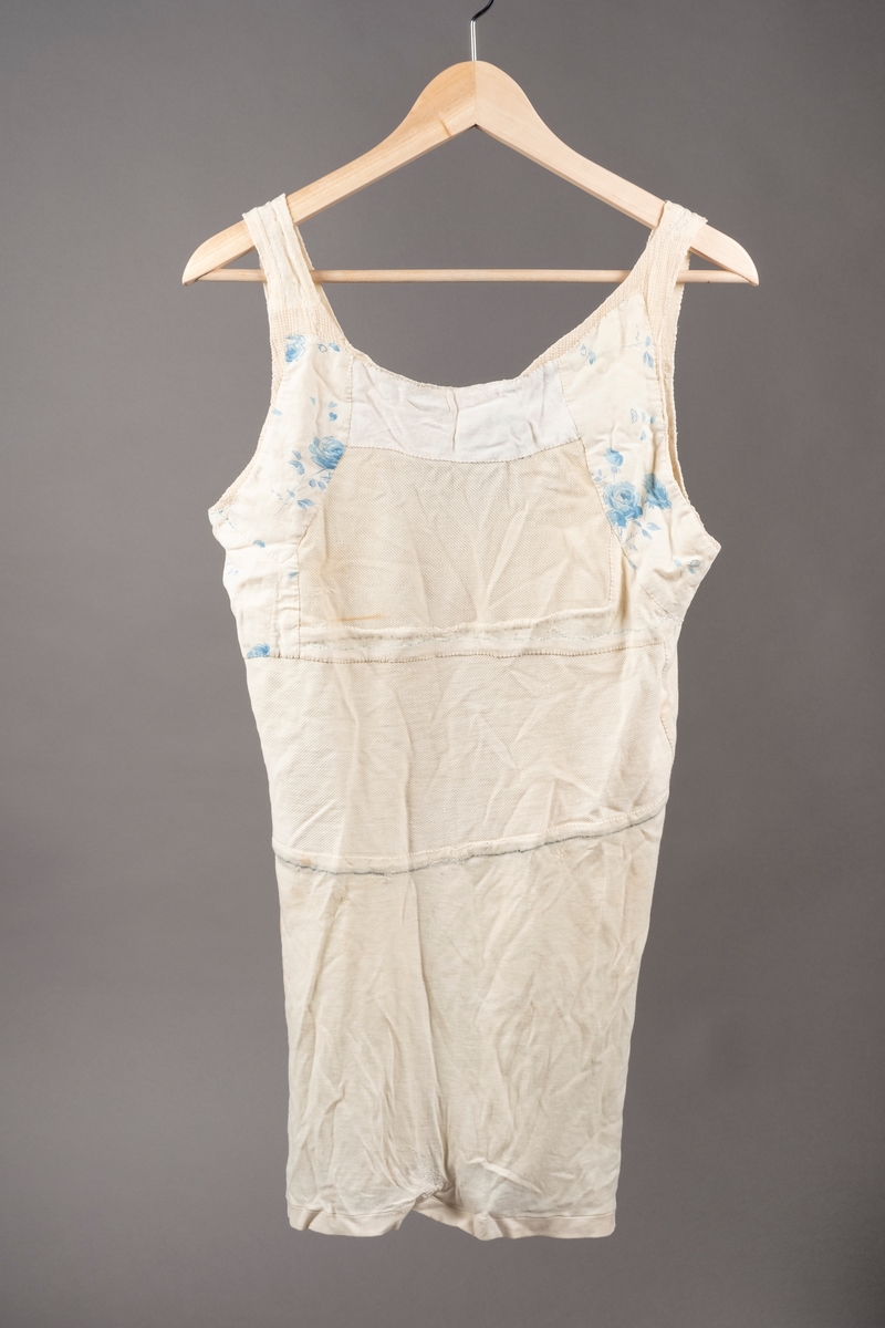 Hvit ullsinglet stoppet og lappet etter skader. Det er brodert inn initialer og navn på ulltrøyen i blå tråd. Noen av lappene har blomstermønstret stoff. Fangenummer er skrevet på i nakken.