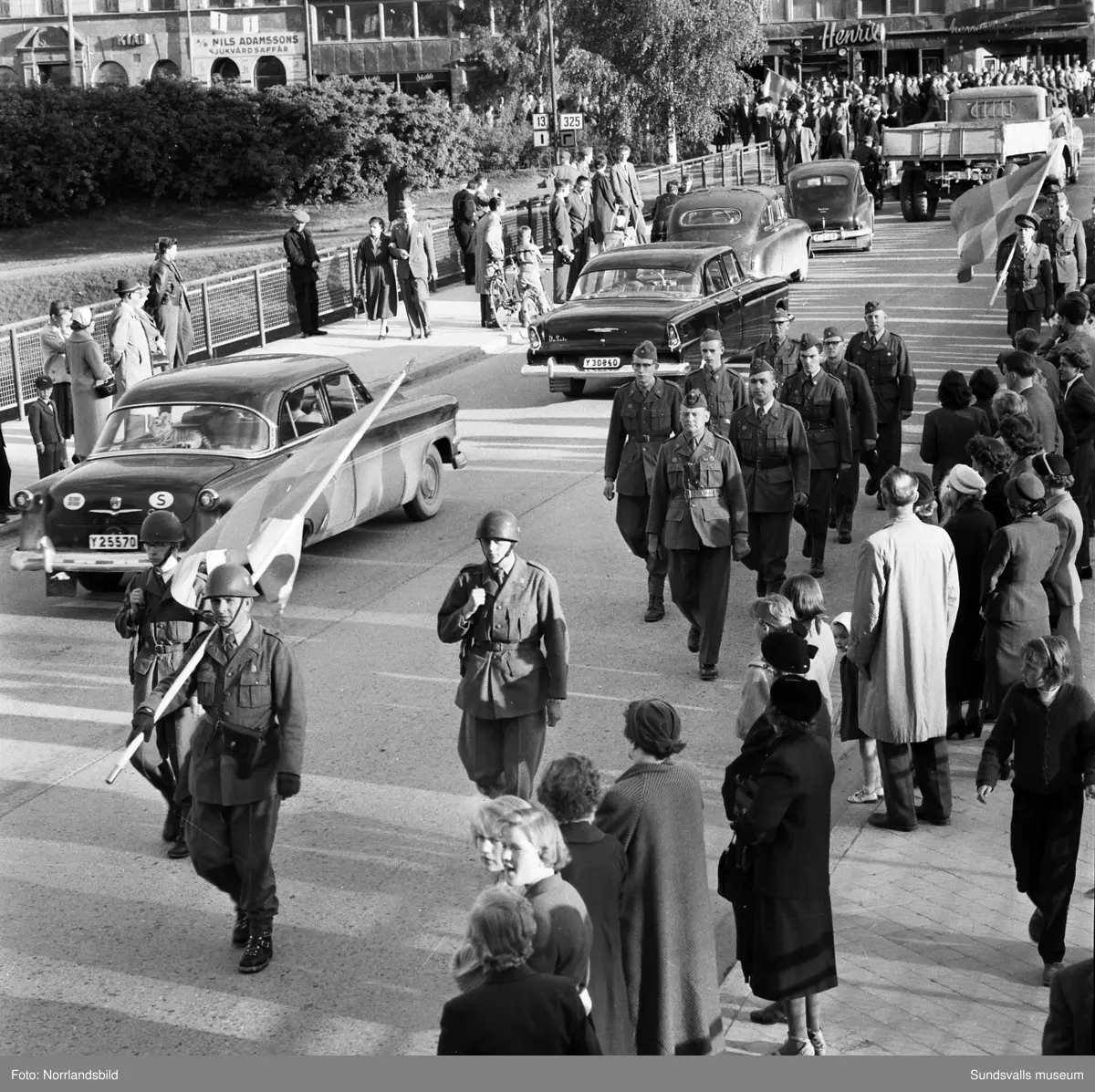 En stor serie bilder från firandet av Svenska flaggans dag 1956. Parad på Storbron med paradorkester, militär, scouter och mängder av olika föreningar och förbund. Därefter högtidlig uppställning i Idrottsparken med bland annat tal, körsång, gymnastikuppvisning och folkmusik.