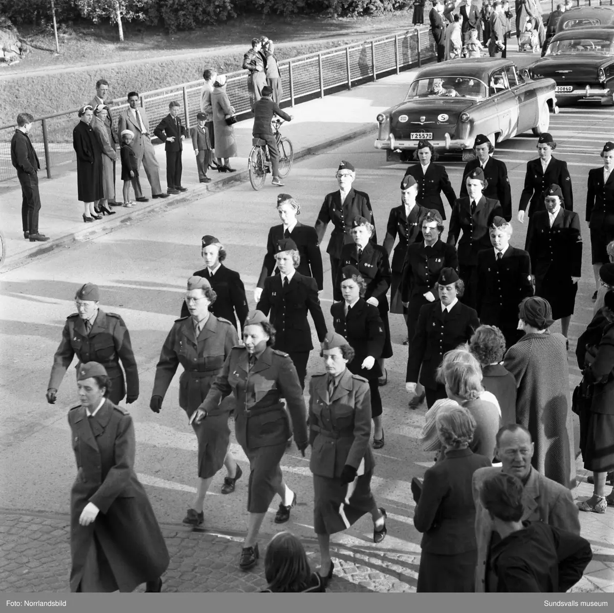 En stor serie bilder från firandet av Svenska flaggans dag 1956. Parad på Storbron med paradorkester, militär, scouter och mängder av olika föreningar och förbund. Därefter högtidlig uppställning i Idrottsparken med bland annat tal, körsång, gymnastikuppvisning och folkmusik.