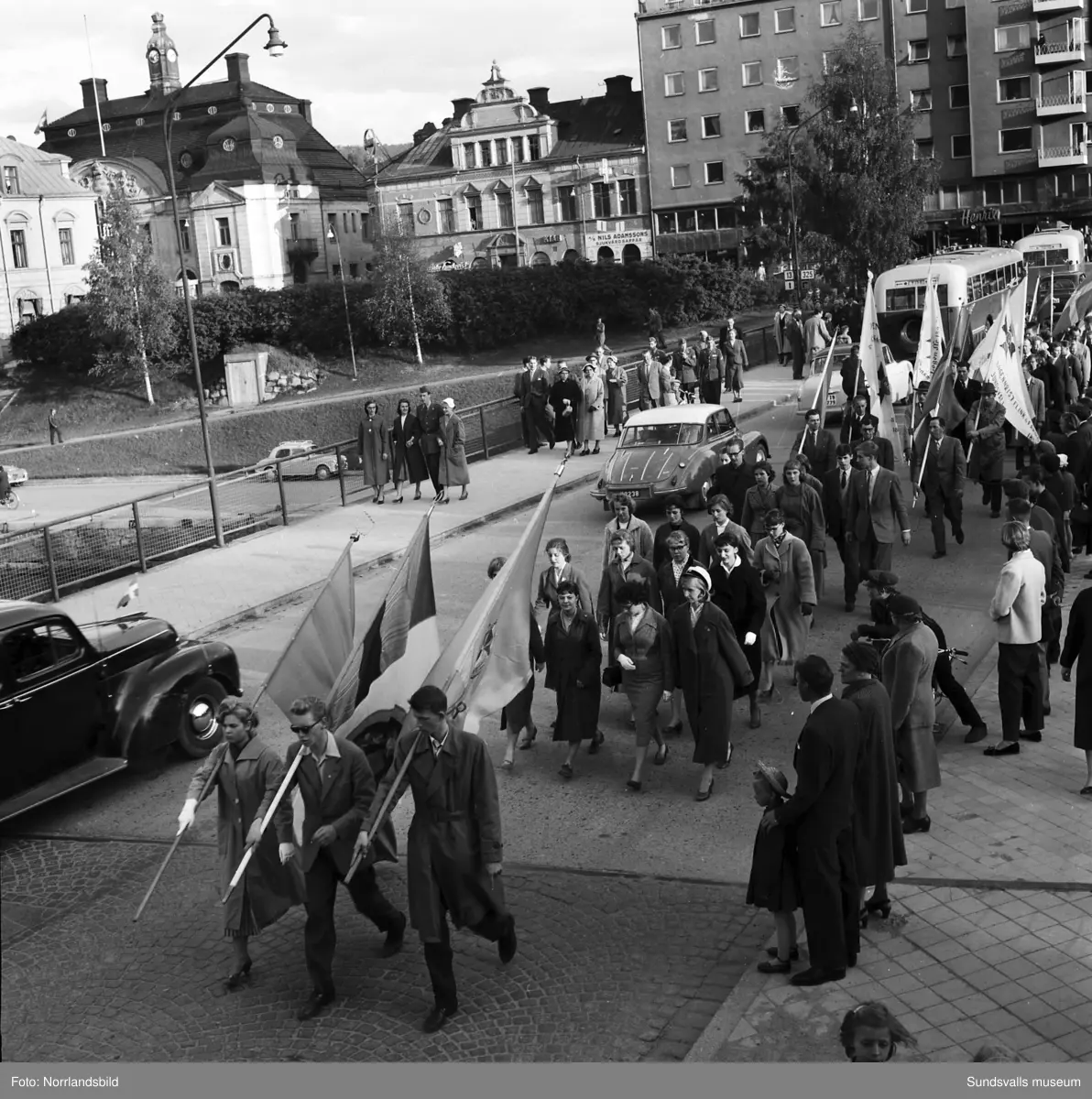 En stor serie bilder från firandet av Svenska flaggans dag 1956. Parad på Storbron med paradorkester, militär, scouter och mängder av olika föreningar och förbund. Därefter högtidlig uppställning i Idrottsparken med bland annat tal, körsång, gymnastikuppvisning och folkmusik.