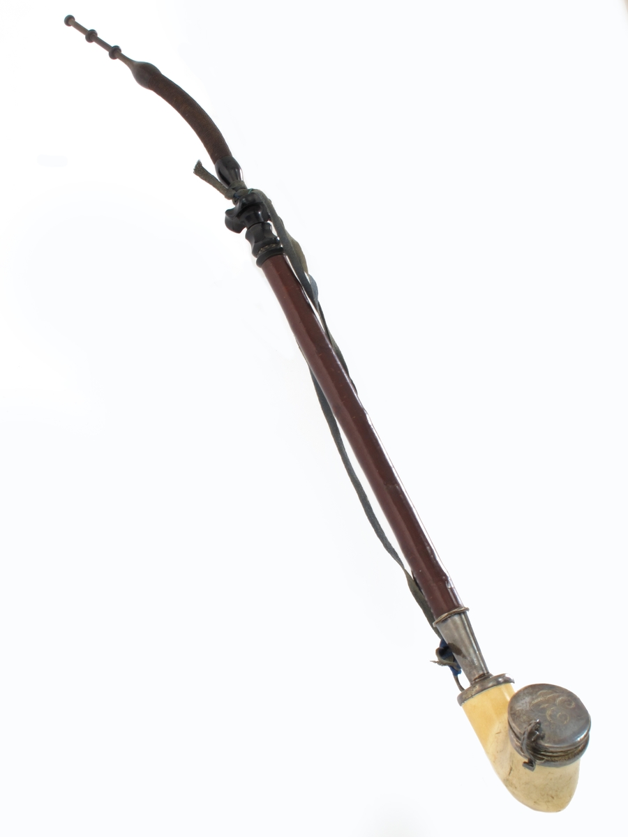 Langpipe med monogram C E (Cristian Eyde). Lys merskum med sølvlokk og beslag. Skaft av  tre  med munnstykke av horn med  flettet tagl. Midtstykke av sort kunststoff. På lokket   inngravert: C E 6/10 99.  Stemplet ved skaftet   P.a. Ø. 830S.  = P.a. Ødegaard Arendal. Fra midt på skaftet til hodet - mørkegrønt (opprinnelig blått)  omullsbånd.  


Om merskum:

Merskum er en massiv form av mineralet sepiolitt, som er et vannholdig magnesiumsilikat. Det oppstår ved forvitring av serpentin.
Merskum danner blekgule eller gråhvite masser som er meget bløte, porøse og flyter på vann, noe som har gitt opphav til navnet. Har en matt, jordlignende overflate som blir blank ved polering.
Merskum er særlig kjent fra Eskisehir i Tyrkia. Materialet brukes til pipehoder og forskjellige prydgjenstander. Forfalskninger er vanlige.
(Kilde: Store Norske leksikon)