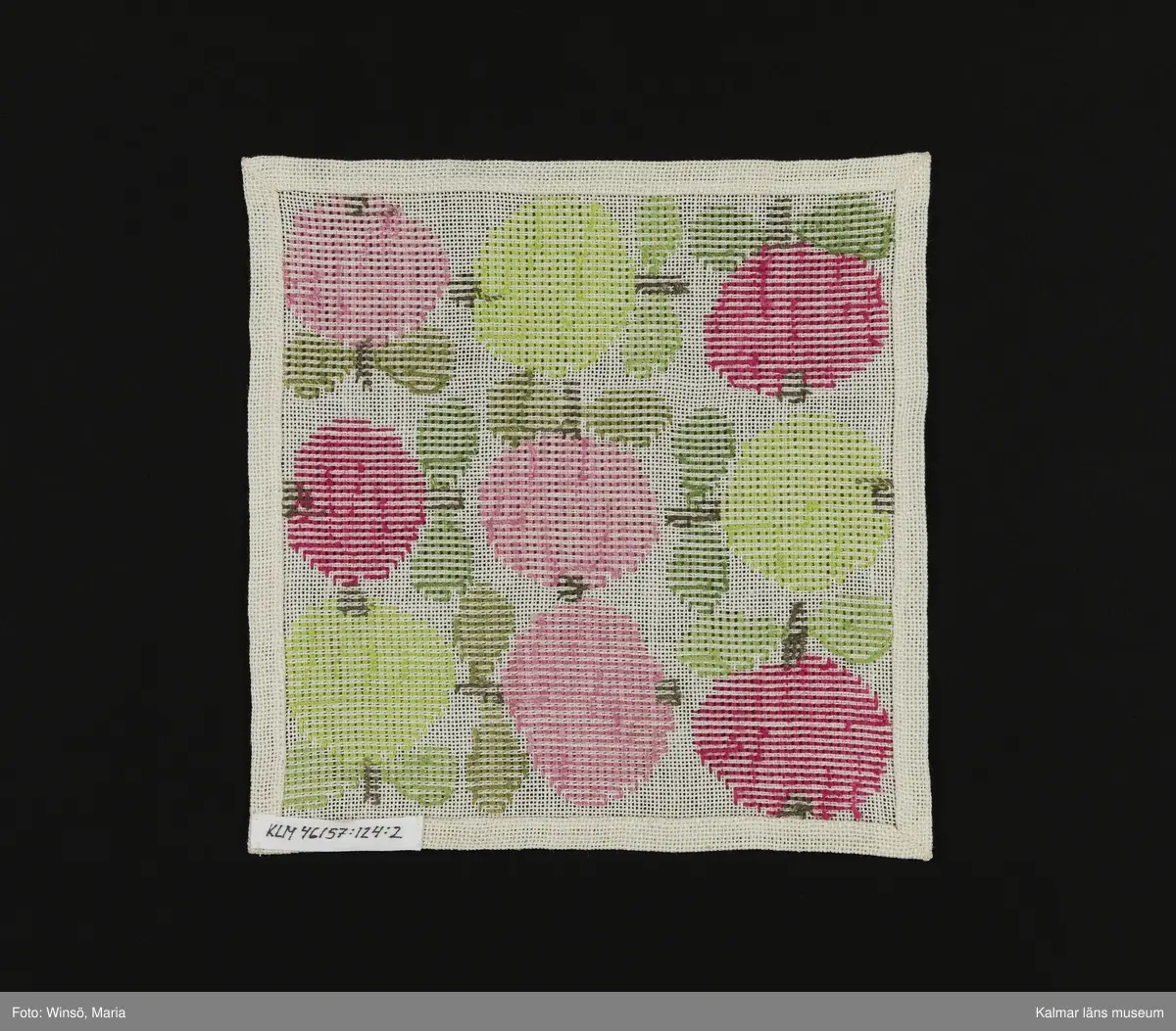 Äppen broderade åt olika håll på vit bakgrund i orange och rosa kulör, med gröna blad (:1) och i rosa och grön kulör med gröna blad (:2). Titel: "Äppelrutan".