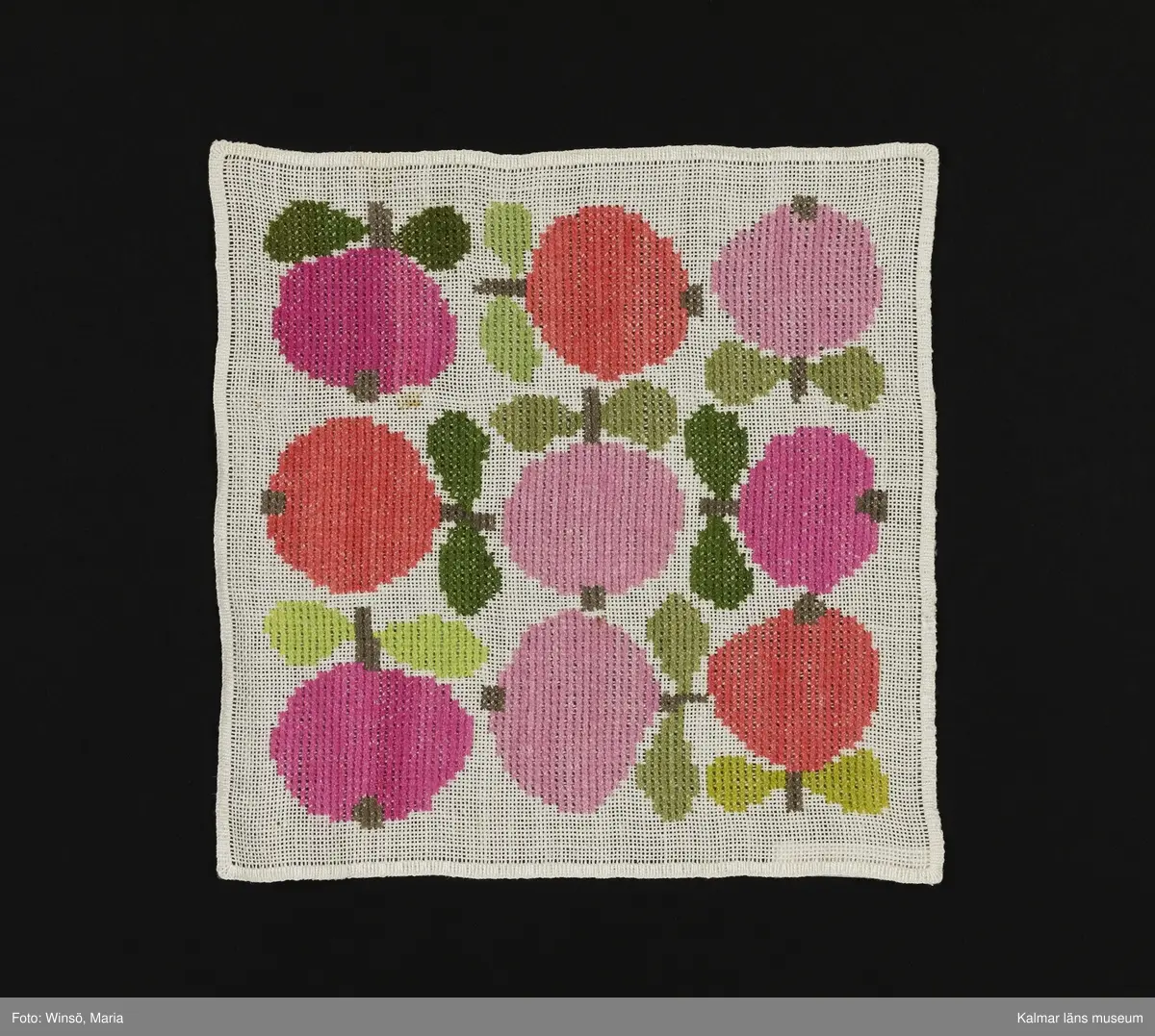 Äppen broderade åt olika håll på vit bakgrund i orange och rosa kulör, med gröna blad (:1) och i rosa och grön kulör med gröna blad (:2). Titel: "Äppelrutan".