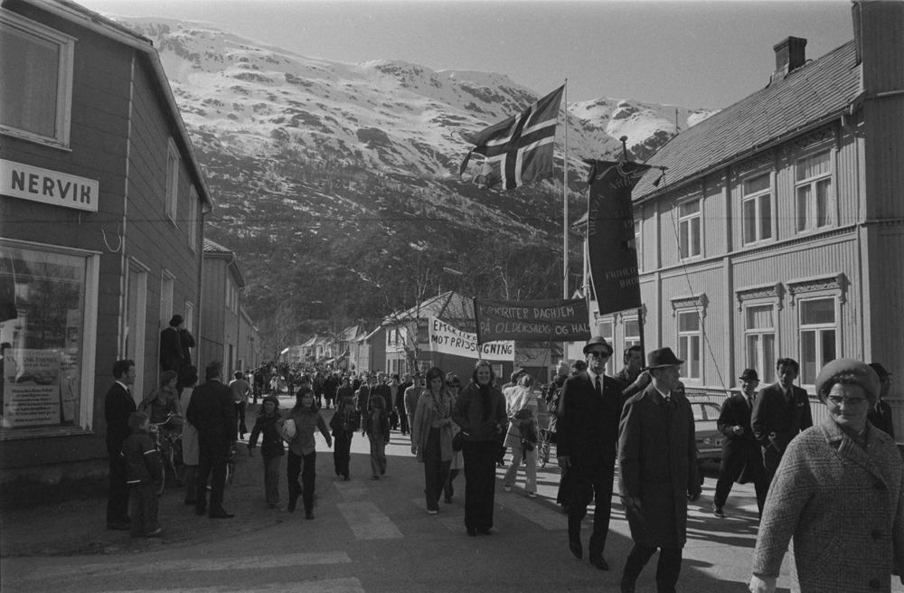 1.Mai i Mosjøen. Demonstrasjonstog kommer oppover Petter Bechsgt. Til høyre IR14 Regimentsgården som ligger i krysset Petter Bechsgt./Kirkegt. 
Til venstre Kåre Nervik bilforretning.(Petter Bechsgt.19)