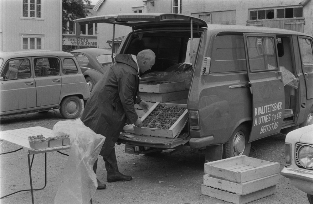 Jordbærsalg på torvet i Mosjøen. Huset til venstre (C.M.Havigsgt. 21) er revet, huset til høyre for Nygaards Farvehandel som vi ser i C.M.Havigsgt. er Wangens Bakeri. De to andre bygningene t.h. ligger i bakgården  mellom Strandgt/C.M.Havigsgt.
Bildet er tatt fra tomta der Gammeltelegrafen sto. (Fokusbygget, Lilletorget etc.)