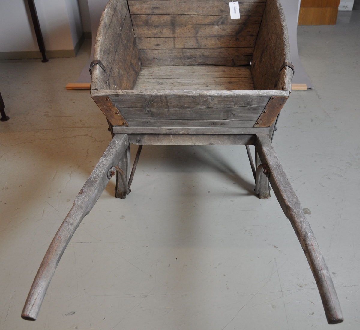 Trillebår av tre og jern. Trillebåren har en ett hjul med påfestet ring av jern, to håndtak og to støttebein. Kassen har utbøyde og avrundede sideplater. I hjørnene av kassen er det armeringer av jern.