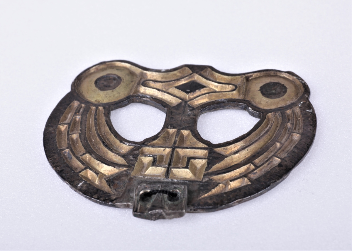 Sølvbeslag og en liten del av dens festeinnretning, forgylt med nielloinnlegg, som type R. 200 d fra eldre jernalder. Utsmykning til sverdslire. Funnet i en gravhaug på gården Mellom-Kvem.