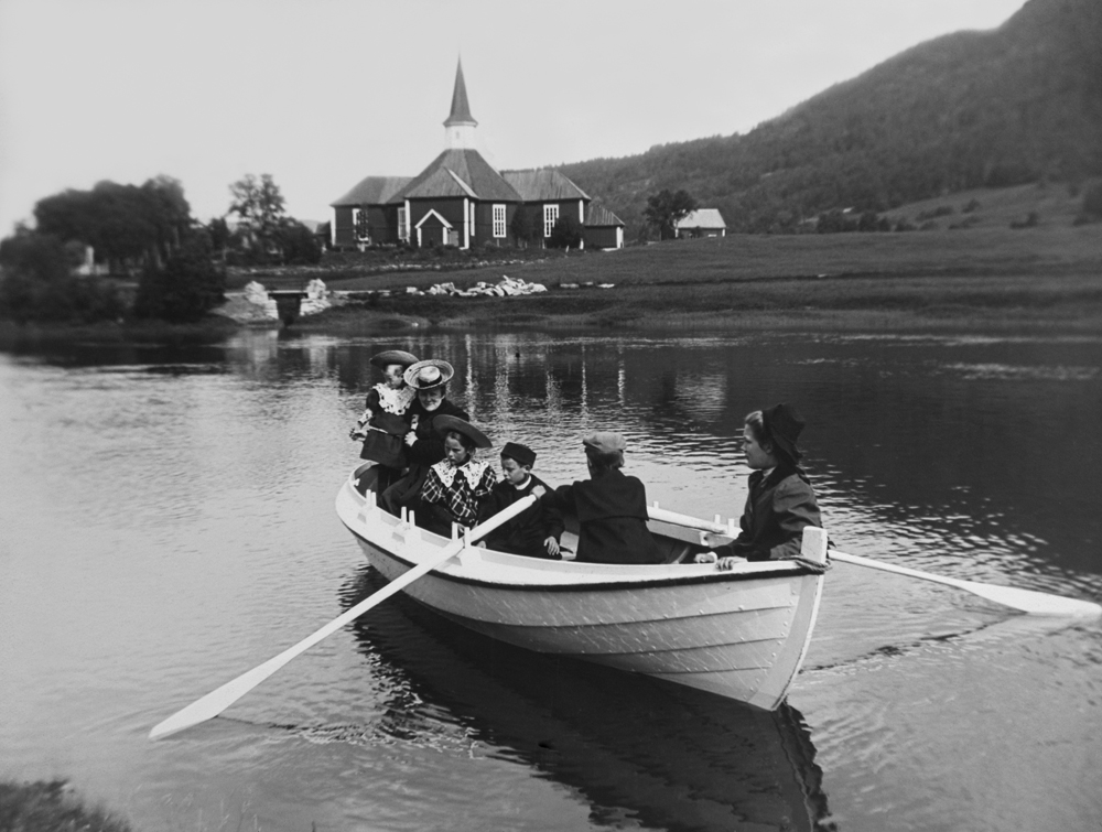 Familien Bakken på rotur i Skjerva 1908. Bak sees Dolstad Kirke. Fra venstre bakerst i båten: Sigrid 5 år, Josefine 46 år, Jorun 9 år, Gunnar 8 år, Odd 14 år, Margitt 16 år.