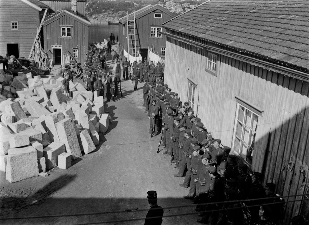 Kleberstein på kommunekaiet. ca.1907-08. T.h.Hellands fruktbutikk. Soldatene står oppstilt for å bli fraktet over til Øyfjellet der de drev skyteøvelse. Større manøver foregikk bl.a. i Kvanndalen. Fra 1912 ble militærvesenet flyttet til Drevja. T.v. store stabler med kleberstein fra Bjørnådalen som skal skippes til Trondheim, til bruk i oppbygginga av Nidarosdomen-"in majorem Dei gloriam".