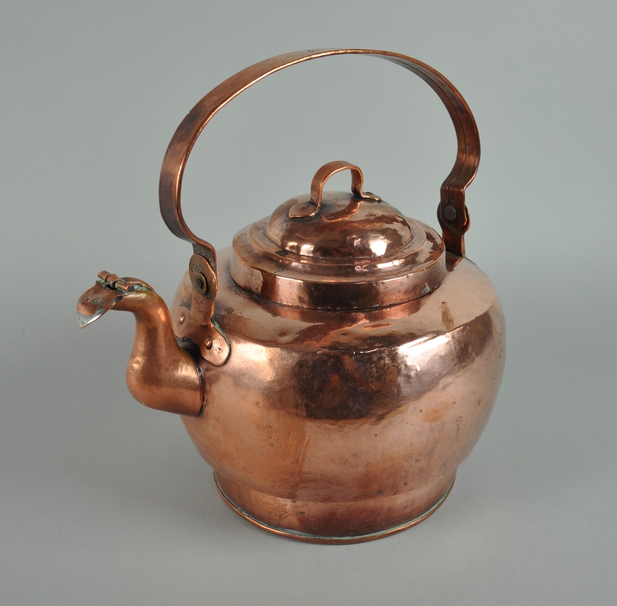 Kjele av kobber. Kjelen har lokk, helletut og hengslet hank som går på tvers over kjelen. I enden av helletuten er det et hengslet lokk. Lokket på kjelen er rundt med påklinket hank.