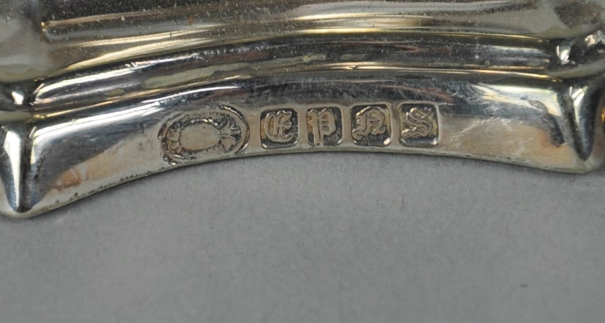 Lysestake av sølv. Lysestaken har firkantet sokkel med rikt profilert dekor. I hjørnene av sokkel er det akantuslignende dekor. På midten av staken er det utgående, akantuslignende dekor.