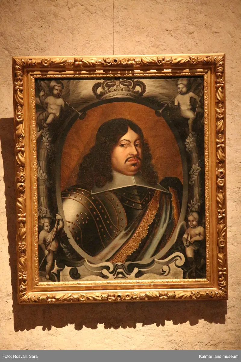 Porträtt, bröstbild av Karl X Gustav i rustning. Vit, stärkt krage, över vänstra axeln ett draperi eller värjgehäng. Oval målad inramning med putti och lagerkransar. Över ovalen en krona, nedan början till textkartusch.